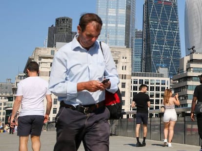 Un hombre utiliza su teléfono móvil, mientras que una mujer toma una fotografía con su smartphone en el London Bridge de la capital británica. 