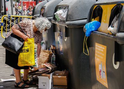 Una señora vacía una bolsa de reciclaje fuera del contenedor.