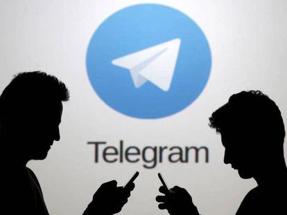 Dos hombres consultan sus teléfonos móviles delante del logotipo de la aplicación Telegram.
 