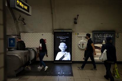 Varias personas pasan delante de una marquesina con el retrato de Isabel II en el metro de Londres. 