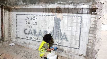 Operaria limpia los azulejos del mural publicitario datado en los años 20.