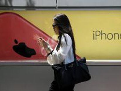 Una mujer utiliza un smartphone mientras camina junto a una publicidad de iPhone 5.