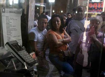 Varios cubanos miran los teléfonos móviles en el escaparate mientras esperan para dar de alta una línea.
