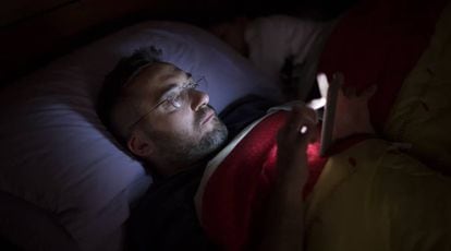 Un hombre lee a oscuras con su smartphone en la cama.