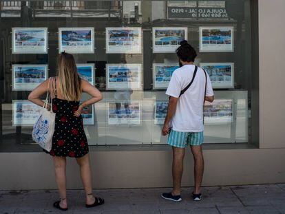 Dos personas observan inmuebles en alquiler y en venta en un escaparate de una inmobiliaria ubicada en Palma de Mallorca