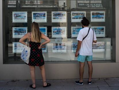 Dos personas observan inmuebles en alquiler y en venta en un escaparate de una inmobiliaria ubicada en Palma de Mallorca