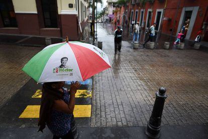 Una mujer camina por una calle del centro de la ciudad de Córdoba con un paraguas promocional del PRI el dí­a 14 de junio de 2018.
