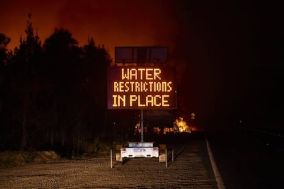 Un letrero indica el mensaje de "Restricción de agua" mientras las llamas arden en el fondo en Lake Tabourie, Australia.