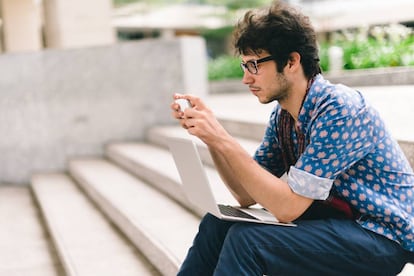 Un jóven utiliza su 'smartphone' y su ordenador.