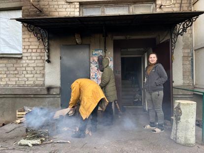 Irina alimenta a hoguera en la que cocina la comida en el portal de su casa, junto a sus hijas, Katya y Kristina, el pasado miércoles.