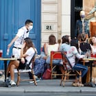 A waiter wearing a face mask serves clients while people eat and have drinks on the terrace of the cafe-restaurant in Paris on June 2, 2020, as cafes and restaurants reopen in France with the easing of lockdown mesures taken to curb the spread of the COVID-19 pandemic, caused by the novel coronavirus. French cafes and restaurants reopened their doors on June 2 as the country took its latest step out of coronavirus lockdown, with clients seizing the chance to bask on sunny terraces after 10 weeks of closures to fight the outbreak.
(Photo by Mehdi Taamallah/NurPhoto via Getty Images)