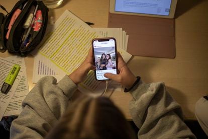 Una estudiante consulta redes sociales en su móvil mientras revisa información por internet.
