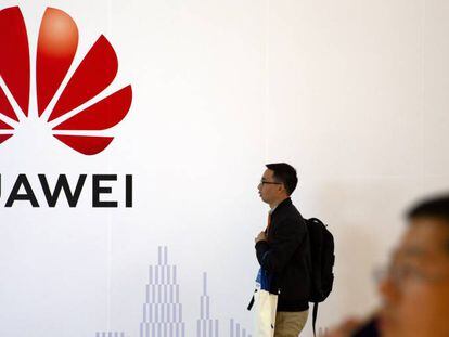 Un hombre pasa junto a un logo de Huawei, mientras otro habla por móvil en una exposición en Pekín.