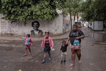 A woman and several children walk in front of a mural by Marielle Franco in Rio de Janeiro.