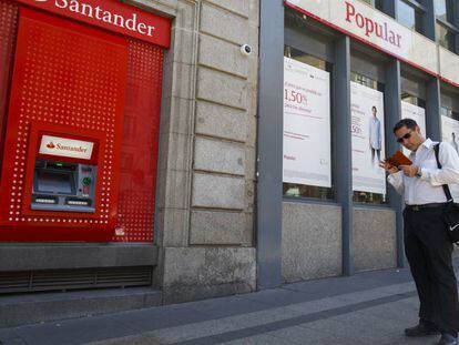 Un hombre pasea junto a una sucursal del Popular y un cajero del Santander.