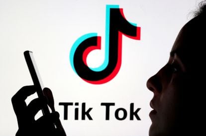 Un joven sostiene su móvil ante un logo de TikTok.
