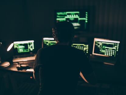 Un hacker sentado frente a un ordenador en una habitación oscura.