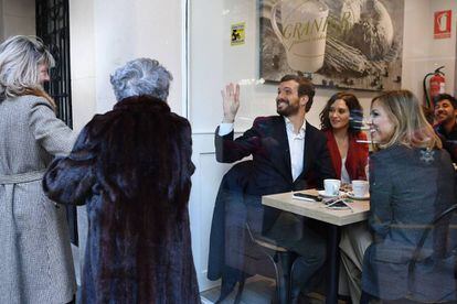 El candidato del PP a las generales, Pablo Casado, sentado junto a la presidenta de la Comunidad de Madrid, Isabel Díaz Ayuso, y su esposa, Isabel Torres, saluda a dos mujeres desde la cafetería donde han desayunado tras votar.