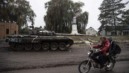 Dos ucranios pasan el día 14 en moto por delante de un tanque ruso en Izium, ciudad recuperada por el ejército de Kiev.