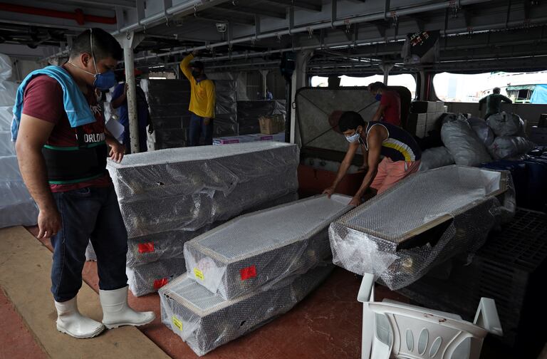 Varios trabajadores desembarcan ataudes llegados este viernes en barco a Manaos desde Santa Catarina.