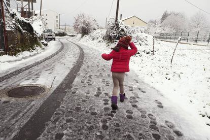 Una niña pasea esta mañana sobre una carretera nevada en el municipio de Palas de Rei (Lugo).
