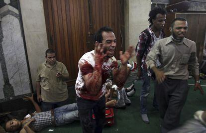 Un egipcio, cuyas manos y ropa est&aacute;n manchadas de sangre, grita en el interior de una mezquita, convertida en un hospital improvisado al que llegan heridos de los disturbios callejeros. 