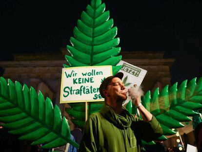 Un hombre fuma frente a un cartel que dice "No queremos ser criminales" en la Puerta de Brandeburgo, en Berlín, la noche del domingo al lunes.