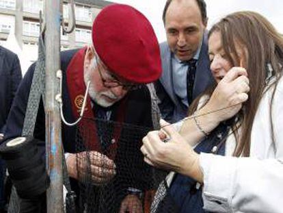 El candidato popular a las elecciones europeas, Miguel Arias Cañete (i), acompañado por el presidente cántabro, Ignacio Diego, observa como cose las redes una pescadora en la Feria, tras ser nombrado cofrade de honor de la Cofradia de la Anchoa, hoy en Santoña.