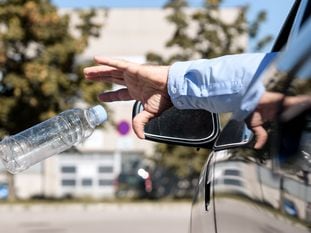 Un hombre arroja una botella de plástico vacía por la ventanilla de su coche.