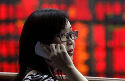 Una agente habla por teléfono frente a una pantalla con los resultados de la Bolsa de Bangkok.