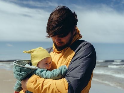 Un padre pasea con su bebé por una playa.