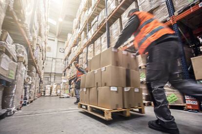 Dos trabajadores del sector logístico trasladan un palé cargado de cajas.
