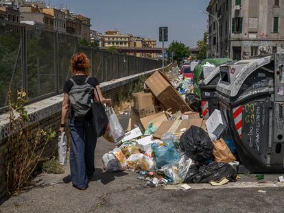 Una mujer camina junto a contenedores de basura desbordados en el barrio del Pigneto de Roma, el 21 de julio.