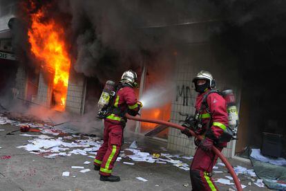 Dos bomberos apagan las llamas de un banco francés tras las protestas en la barriada de Nanterre, este jueves. 