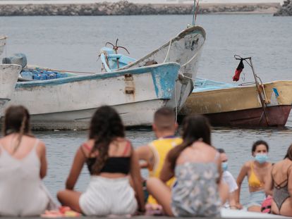 Bañistas frente a los cayucos amontonados en el muelle de Arguineguín, en Gran Canaria, donde han llegado a pernoctar bajo carpas más de 400 inmigrantes.