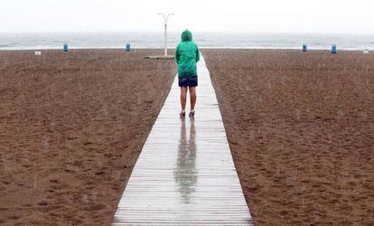 Una mujer contempla la playa de la Malvarrosa bajo la lluvia.