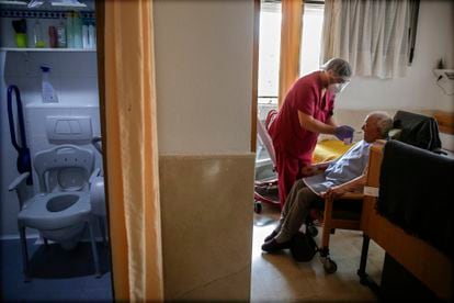 Un empleado cuida de un hombre mayor en una de las habitaciones en la residencia de ancianos Santa María de Montecarmelo, en Madrid.