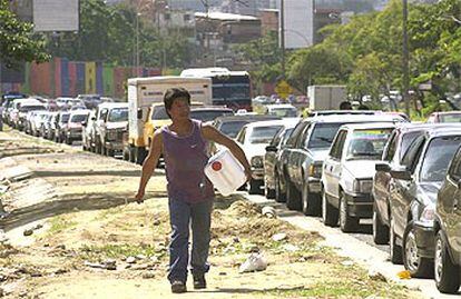 Un hombre camina con un bidón hacia una gasolinera de Caracas ante una cola de coches que van a repostar.
