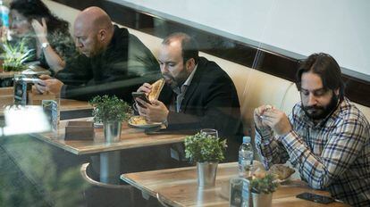 Cuatro personas comen en un restaurante con sus teléfonos móviles en la mesa.