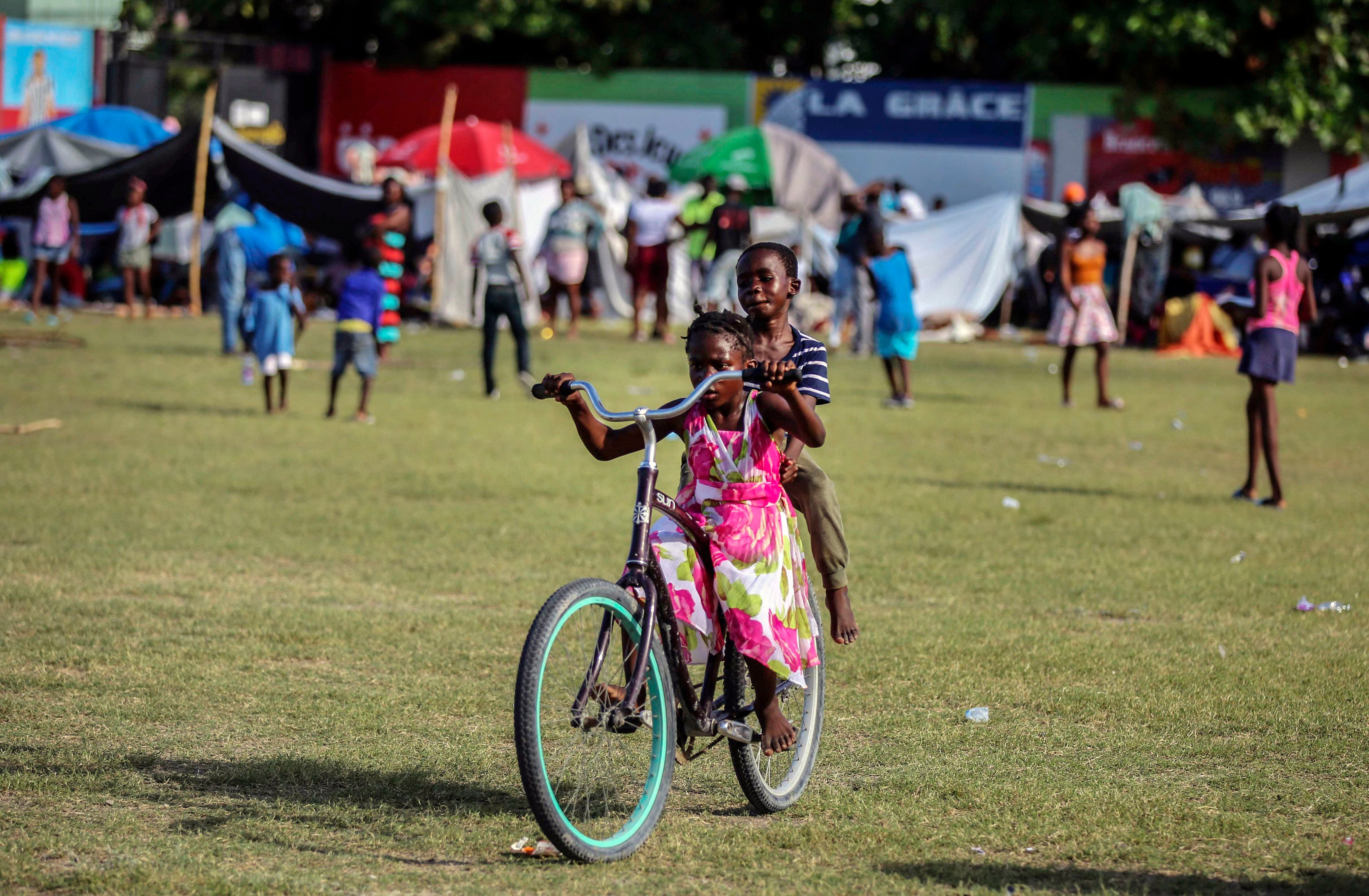 Niños afectados por el terremoto juegan en bicicleta en un campamento de refugiados en Los Cayos, Haití, el domingo 15 de agosto de 2021.