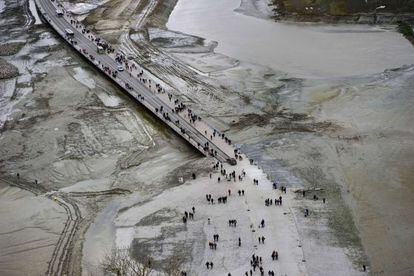 Turistas y curiosos esperan la subida de la marea en la carretera que se dirige al Mont Saint Michel.