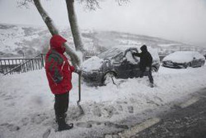 Dos personas intentan despejar su coche de nieve en la zona entre A Canda (Ourense) y Padornelo (Zamora).