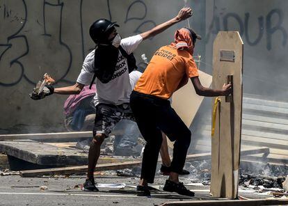 Dos manifestantes  protegidos con escudos caseros se enfrentan a la policía durante el paro nacional convocado por la oposición.