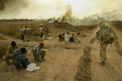 30 de marzo de 2003. Varios soldados del 40º comando Real de Marines británico, esposan a milicianos iraquíes prisioneros, tras su rendición, mientras en la parte trasera de la imagen un carro de combate T-55 de fabricación rusa, arde, en Abu Al Khasib, un suburbio de Basora.