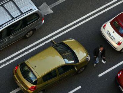 Un peat&oacute;n cruza la calzada entre coches en la Gran V&iacute;a de Madrid.