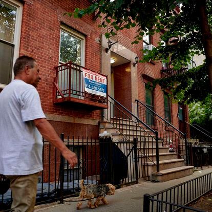 Un hombre pasea a su perro en el East Village de Nueva York junto a un cartel de se alquila piso.