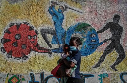 Una mujer con un bebé en brazos pasa delante de un mural que simboliza la lucha contra el coronavirus en una calle de Kericho, Kenia.