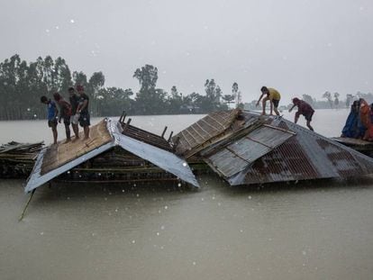 Varios afectados por las inundaciones cargan trozos de sus casas en una barca en Kurigram, Bangladesh, el pasado 27 de julio. En vídeo, el reportaje.
