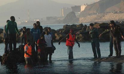 Unos guardias civiles ayudan a los inmigrantes llegados esta mañana a la playa ceutí de Tarajal.