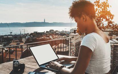 Una mujer trabaja con su ordenador en una terraza de Lisboa con vistas al Tajo.